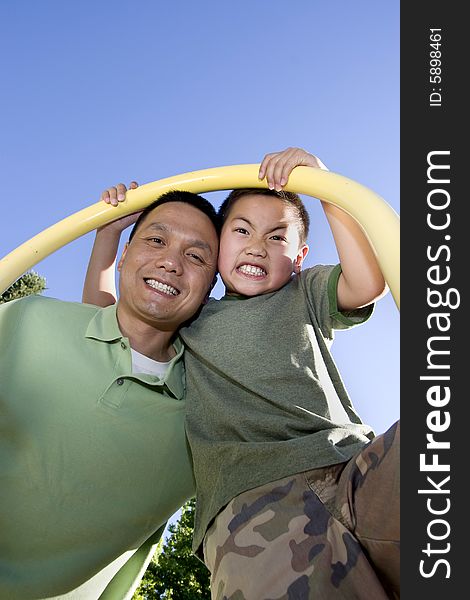 Father and son stand beneath fireman's pole on jungle gym. Father and son are looking down and smiling at the camera. Vertically framed photo. Father and son stand beneath fireman's pole on jungle gym. Father and son are looking down and smiling at the camera. Vertically framed photo.