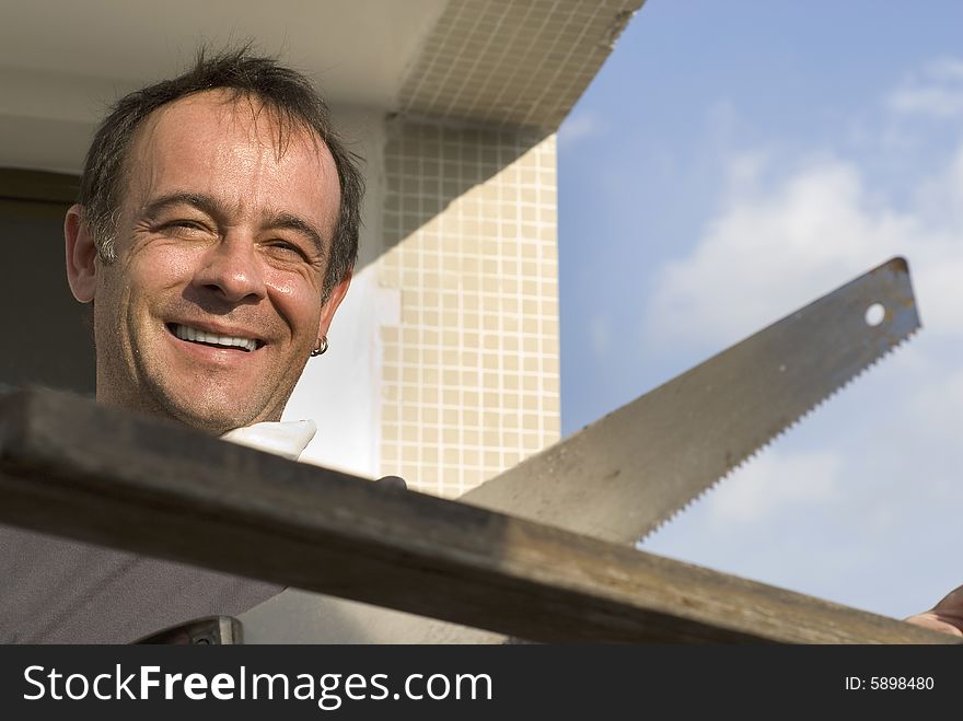 A man, stands smiling, sawing a piece of wood. Horizontally framed shot. A man, stands smiling, sawing a piece of wood. Horizontally framed shot.
