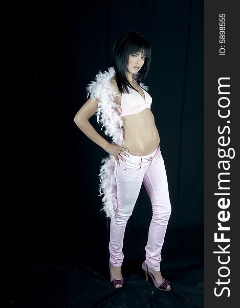 Full length of a young woman dressed in pink denims, a pink top and boa and purple shoes. She has black hair and pink lipstick. Full length of a young woman dressed in pink denims, a pink top and boa and purple shoes. She has black hair and pink lipstick.