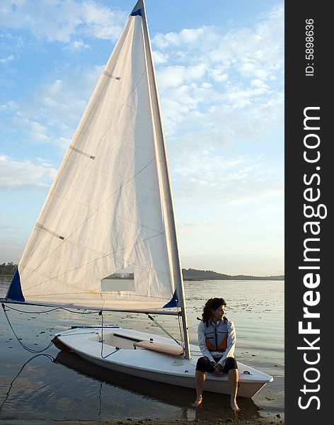 A woman is sitting on a sailboat in the water.  She is relaxed, smiling, and looking away from the camera.  Vertically framed shot. A woman is sitting on a sailboat in the water.  She is relaxed, smiling, and looking away from the camera.  Vertically framed shot.