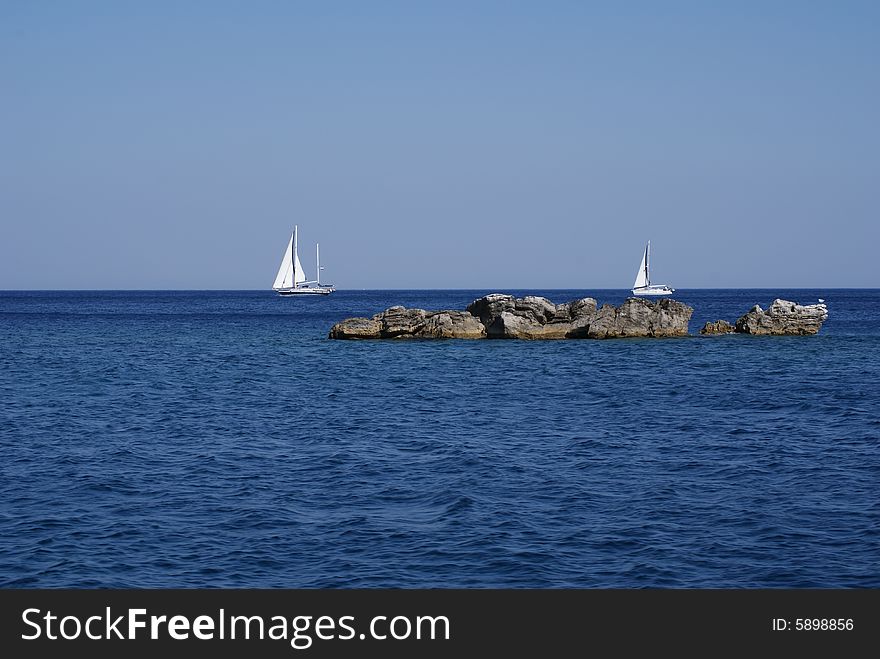 Two sailboats behind the rocks. Two sailboats behind the rocks
