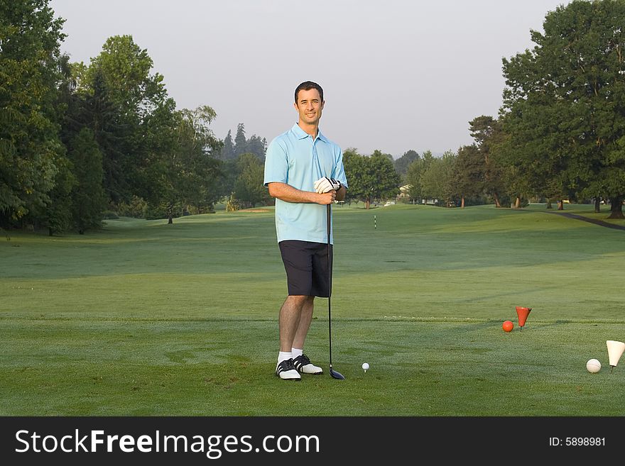 Male golfer casually standing on green holding golf club. Horizontal framed shot. Male golfer casually standing on green holding golf club. Horizontal framed shot.