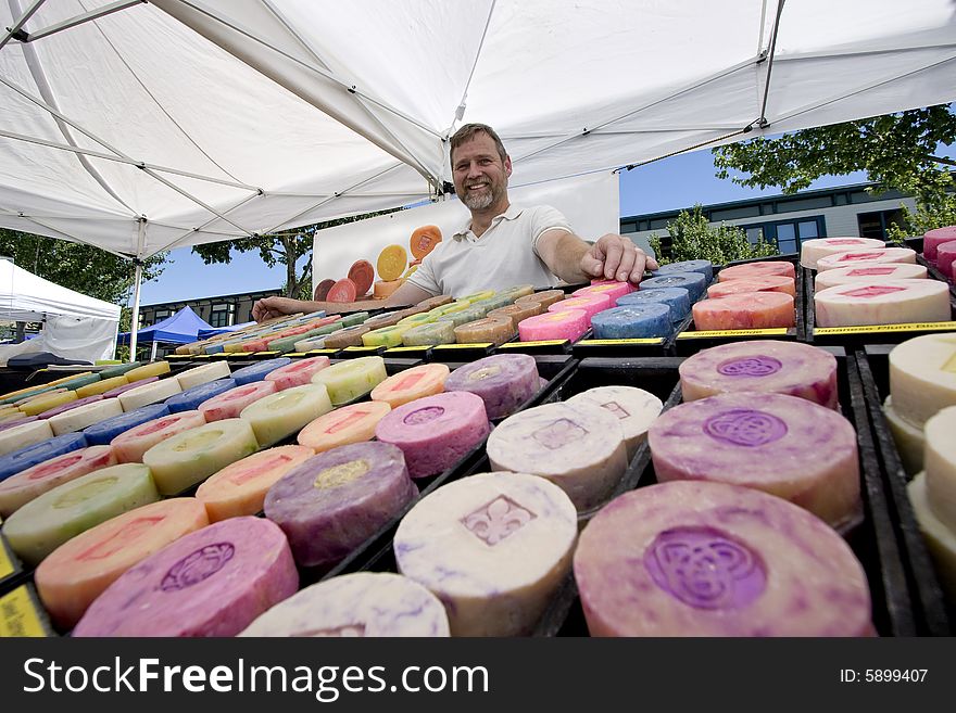 Man with beard standing behind rows of soap displaying soap for sale. Soal is of varying colors. Horizontally framed photo. Man with beard standing behind rows of soap displaying soap for sale. Soal is of varying colors. Horizontally framed photo.