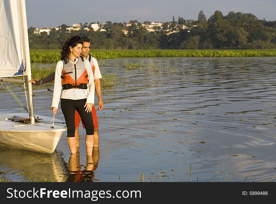 Smiling man and woman standing in shallow water holding sailboat and looking across lake. Horizontally framed photo. Smiling man and woman standing in shallow water holding sailboat and looking across lake. Horizontally framed photo