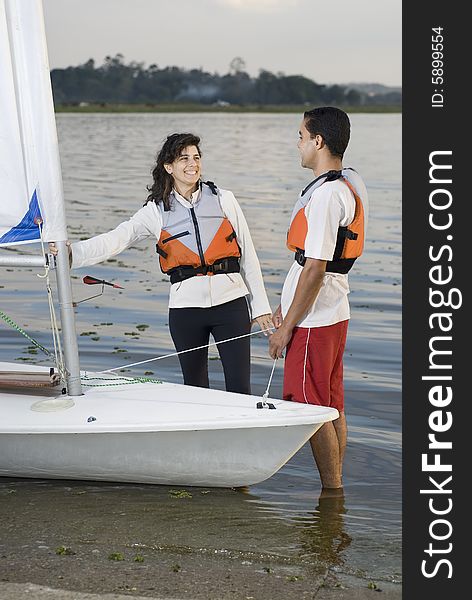 Smiling man and woman standing next to  sailboat looking at eachother. Vertically framed photo. Smiling man and woman standing next to  sailboat looking at eachother. Vertically framed photo
