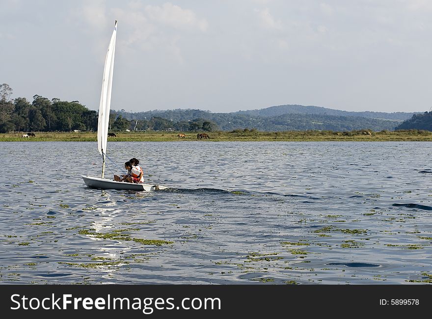 Couple sailing on sailboat in the distance. Sailing across lake. Horizontally framed photo. Couple sailing on sailboat in the distance. Sailing across lake. Horizontally framed photo