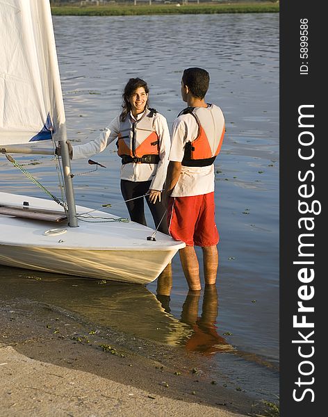 Man and woman standing in shallow water next to sailboat talking. Vertically framed photo. Man and woman standing in shallow water next to sailboat talking. Vertically framed photo.