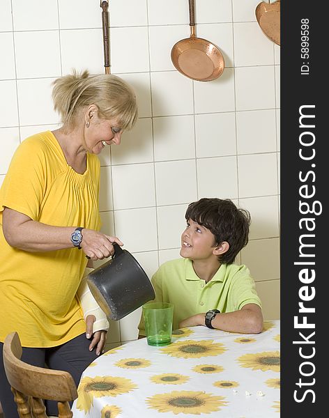 Woman standing next to table pouring drink into glass for seated child. Vertially framed photo. Woman standing next to table pouring drink into glass for seated child. Vertially framed photo.