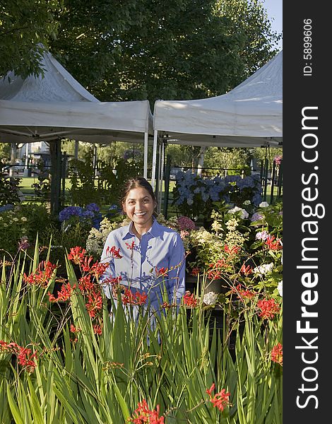 Woman standing behind flowers smiling at camera. Vertically framed photo. Woman standing behind flowers smiling at camera. Vertically framed photo.