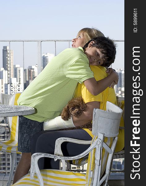 Boy standing while hugging seated woman. Woman wearing cast and holding dog. Vertically framed photo. Boy standing while hugging seated woman. Woman wearing cast and holding dog. Vertically framed photo.