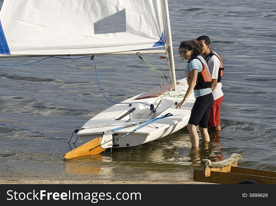 Man and woman standing in shallow water launching sailboat. Horizontally framed photo. Man and woman standing in shallow water launching sailboat. Horizontally framed photo