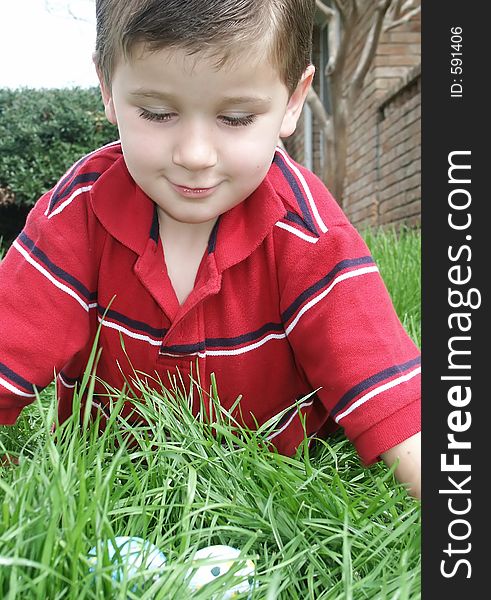 A young boy leaning over decorated Easter eggs he has found in the grass. A young boy leaning over decorated Easter eggs he has found in the grass.