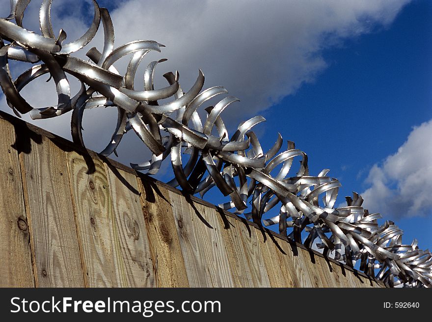 Razor wire on top of fence against a blue sky. Razor wire on top of fence against a blue sky.