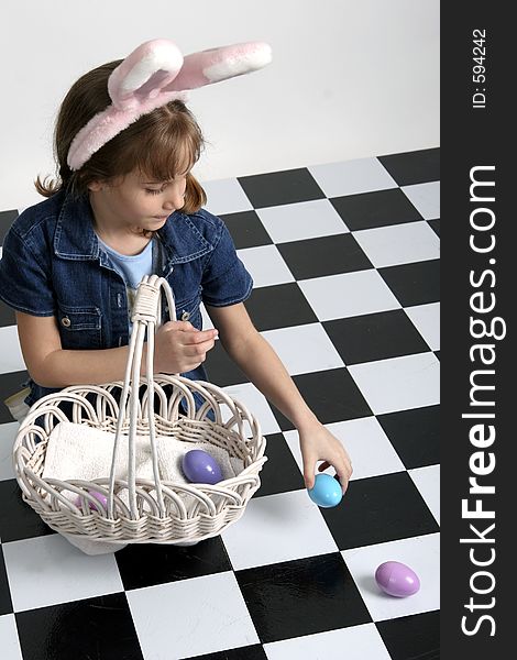 Little girl in Easter bunny ears picking up eggs and putting them in a basket. Little girl in Easter bunny ears picking up eggs and putting them in a basket.