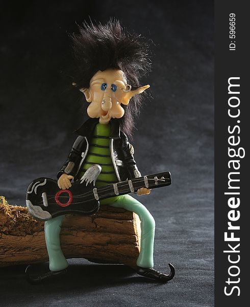 Rocker dwarf playing the guitar sat on a trunk. Black background. Punk hair