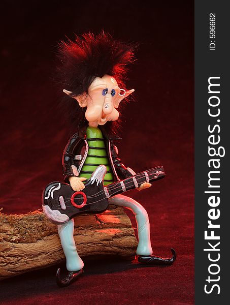 Rocker dwarf playing the guitar sat on a trunk. Red lighting