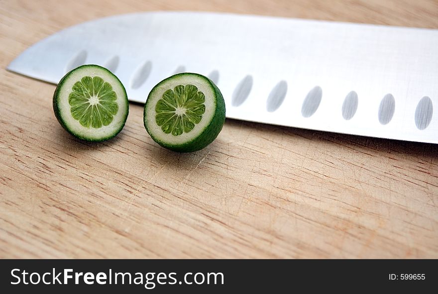 Tiny baby lime on cutting board with chef's knife. Strange perspective with tiny lime and large knife. Tiny baby lime on cutting board with chef's knife. Strange perspective with tiny lime and large knife.