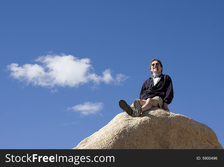 A hiker surveys his world while sitting on the top of a rock on a sunny day in Joshua Tree National Park. A hiker surveys his world while sitting on the top of a rock on a sunny day in Joshua Tree National Park.