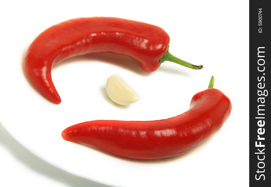 Two fresh chili peppers and a skinless clove of garlic on a white plate and isolated on white background. Two fresh chili peppers and a skinless clove of garlic on a white plate and isolated on white background