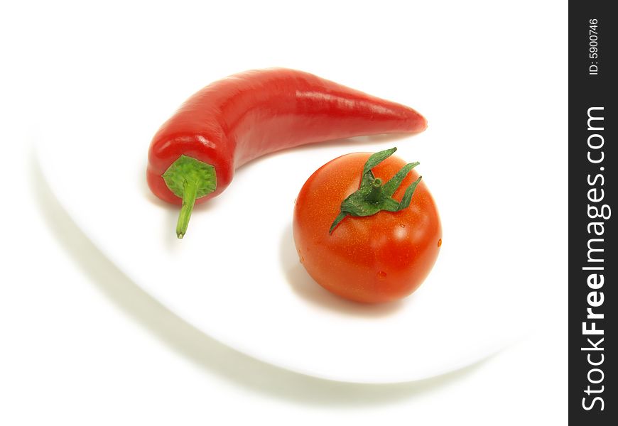 A fresh tomato and a ripe chili pepper on a white plate and isolated on white background. A fresh tomato and a ripe chili pepper on a white plate and isolated on white background