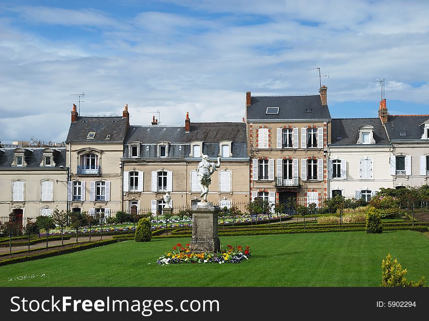 Smart street against the blue cloudy sky, spring french park with green lawn, bright flower-beds, sculptures in the foreground. Smart street against the blue cloudy sky, spring french park with green lawn, bright flower-beds, sculptures in the foreground