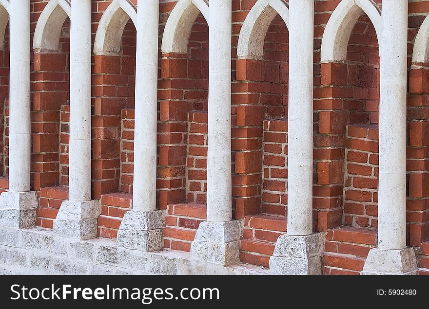 A row of stone columns against red brick wall. Tsaritsino park in Moscow.