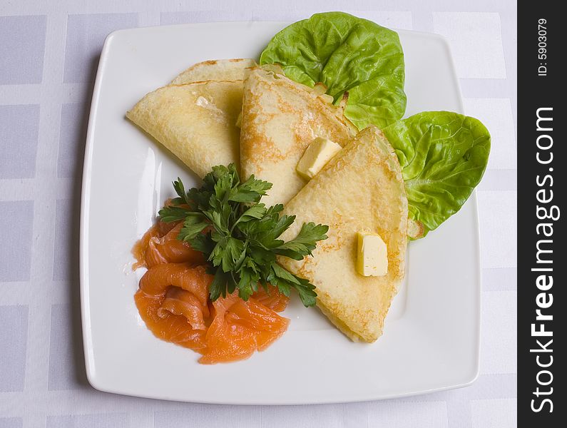 Pancakes with salty salmon on white plate on white ground