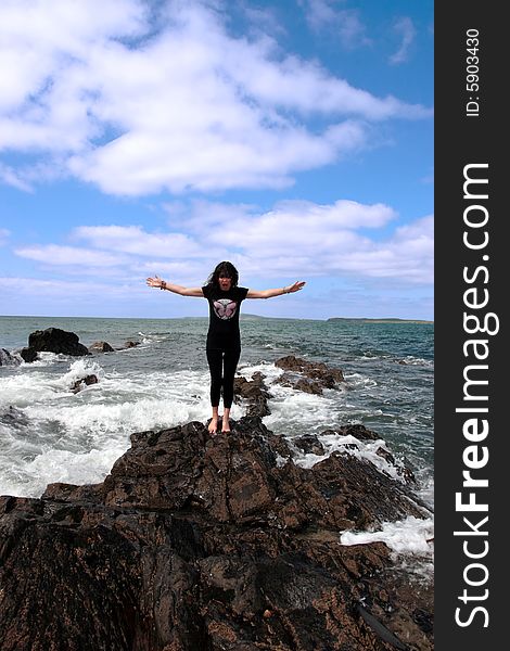 A beautiful woman doing yoga on the edge of the rocks with waves splashing to show a healthy way to live a happy and relaxed lifestyle in a world full of stress. A beautiful woman doing yoga on the edge of the rocks with waves splashing to show a healthy way to live a happy and relaxed lifestyle in a world full of stress