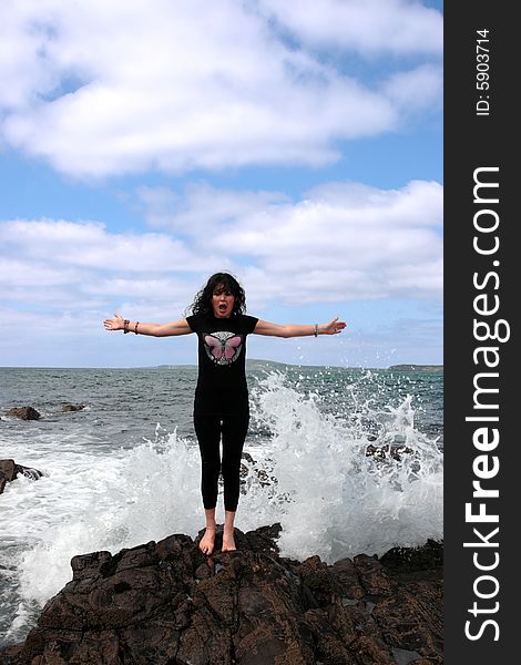 A beautiful woman doing yoga on the edge of the rocks with waves splashing to show a healthy way to live a happy and relaxed lifestyle in a world full of stress. A beautiful woman doing yoga on the edge of the rocks with waves splashing to show a healthy way to live a happy and relaxed lifestyle in a world full of stress