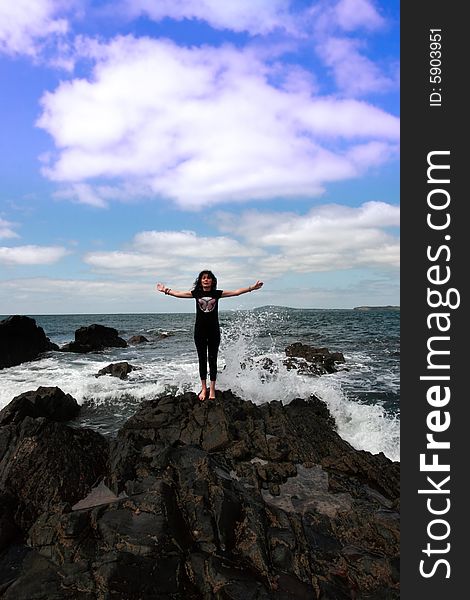 A beautiful woman doing yoga on the edge of the rocks with waves splashing to show a healthy way to live a happy and relaxed lifestyle in a world full of stress. A beautiful woman doing yoga on the edge of the rocks with waves splashing to show a healthy way to live a happy and relaxed lifestyle in a world full of stress