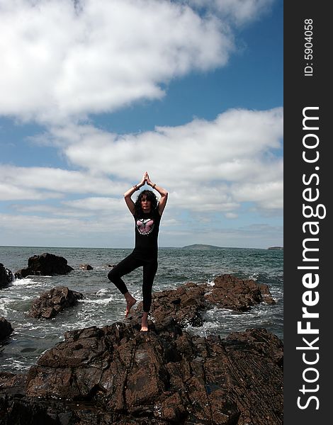 A beautiful woman doing yoga on the edge of the rocks with waves splashing to show a healthy way to live a happy and relaxed lifestyle in a world full of stress. A beautiful woman doing yoga on the edge of the rocks with waves splashing to show a healthy way to live a happy and relaxed lifestyle in a world full of stress