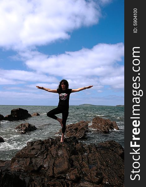 A beautiful woman doing yoga on the edge of the rocks with waves splashing to show a healthy way to live a happy and relaxed lifestyle in a world full of stress. A beautiful woman doing yoga on the edge of the rocks with waves splashing to show a healthy way to live a happy and relaxed lifestyle in a world full of stress