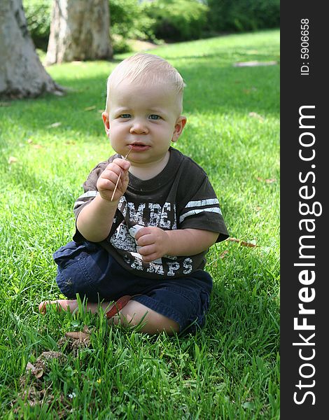 Child toddler is sitting while chewing on a piece of grass. Child toddler is sitting while chewing on a piece of grass