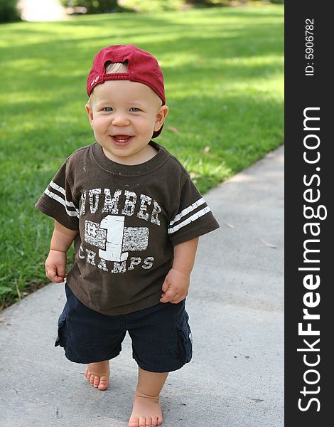 Child toddler is standing on a path in with a baseball cap and smiling. Child toddler is standing on a path in with a baseball cap and smiling.