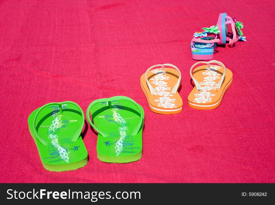 Three pairs of flipflops on red beachtowel. Symbol for dad, mum and the little daughter. Family on vacation, fun, sea and summer concept. Space for copy.