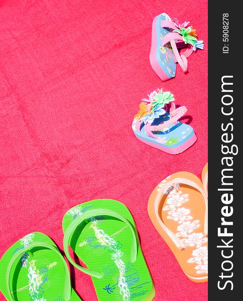Three pairs of flipflops on red beachtowel. Symbol for dad, mum and the little daughter. Family on vacation, fun, sea and summer concept. Space for copy.