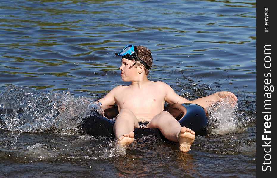 The boy sitting on a tube making splashes in a small lake.