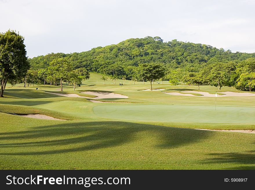 A green and fairway on a golf course in a tropical setting. A green and fairway on a golf course in a tropical setting