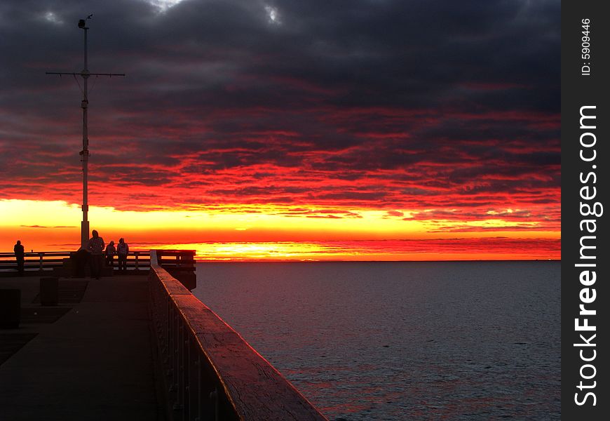 Orange clouds as the sun rises over the ocean with pier in foreground. Orange clouds as the sun rises over the ocean with pier in foreground