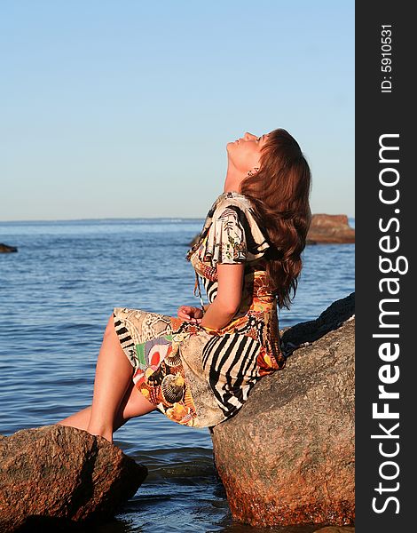 Young lady sitting on a stone and looking up to the skies. Young lady sitting on a stone and looking up to the skies