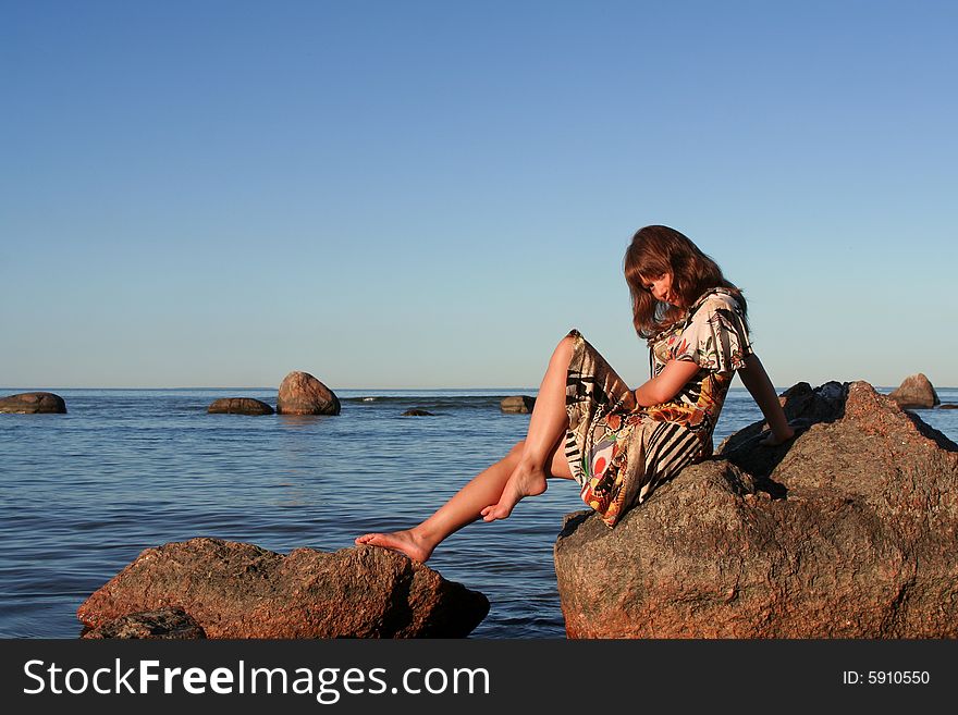 Pretty young woman sitting on a stone in the sea