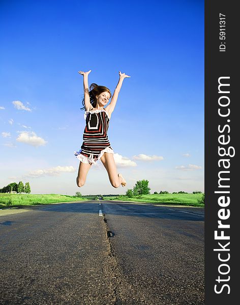 Jumping happy girl over the road under blue sky