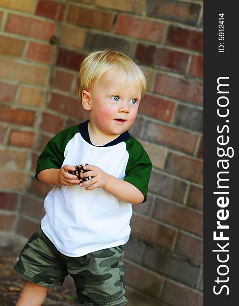 A little boy outside with a pine cone he found