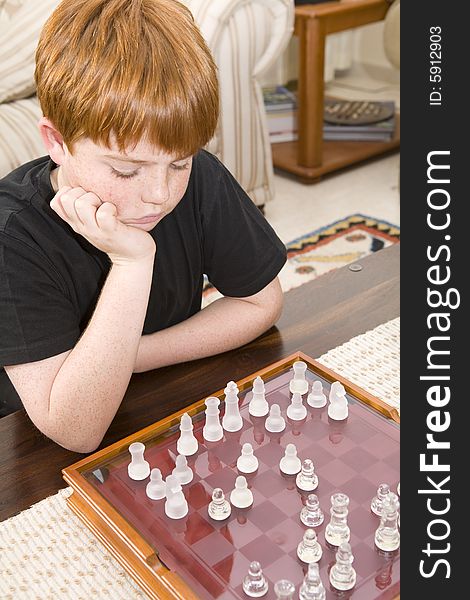 A ten year old boy with red hair playing chess indoors. A ten year old boy with red hair playing chess indoors