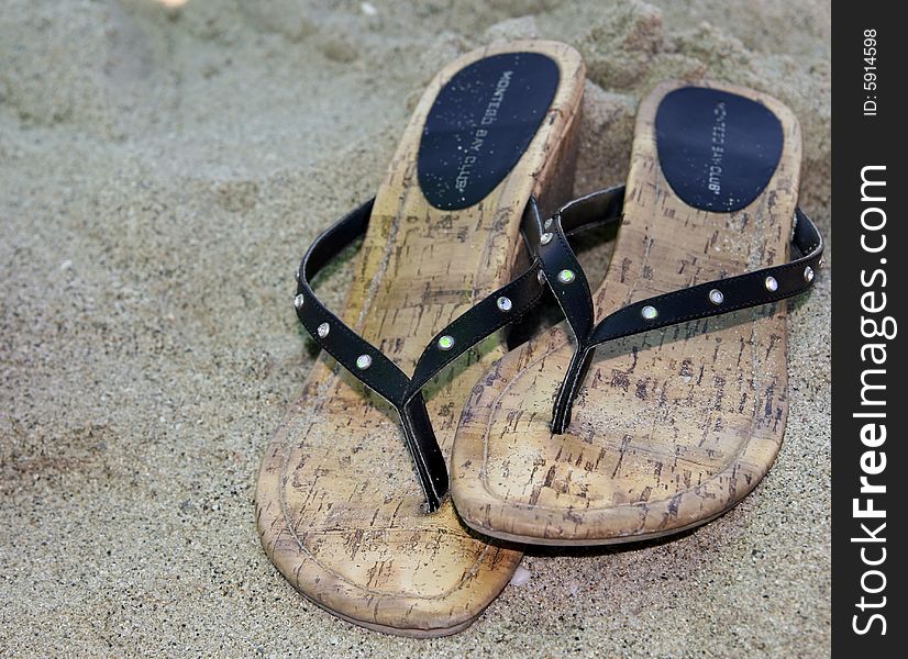 A pair of black sandals on a sandy beach. A pair of black sandals on a sandy beach