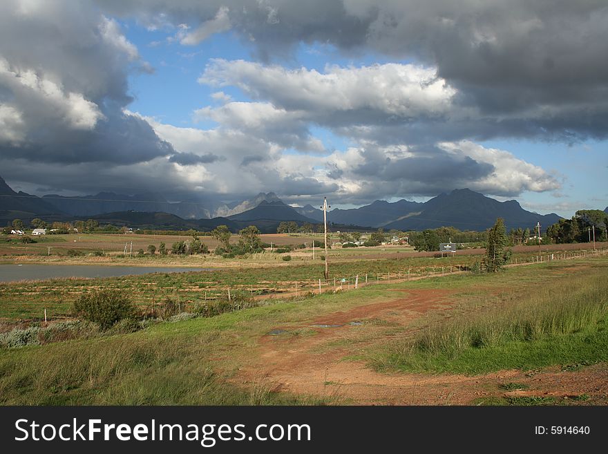 Landscape of many colour contrasts. Stormy sky with green fields and blue mountains in the background. Landscape of many colour contrasts. Stormy sky with green fields and blue mountains in the background