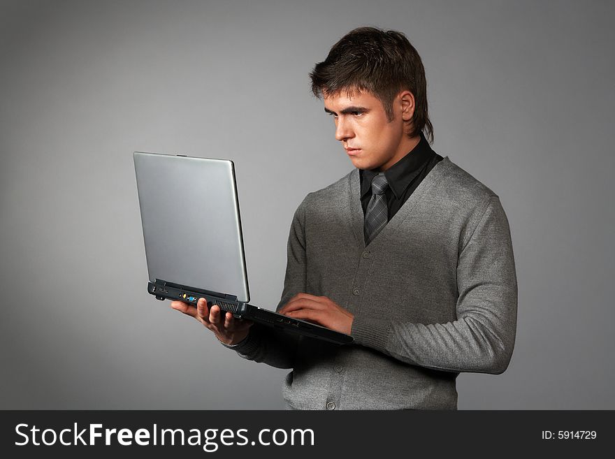 Young businessman is holding laptop and typing isolated on gray