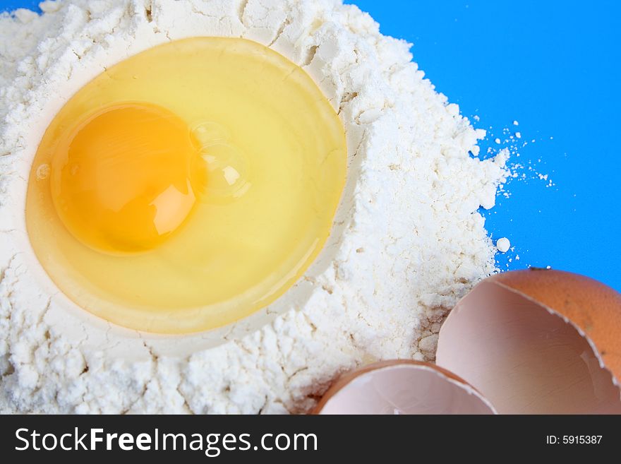 Raw egg in flower with egg shells, against a blue background. Raw egg in flower with egg shells, against a blue background