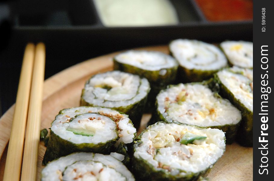 Close-up of maki sushi rolls arranged on a plate with chopsticks, dips blurred in background.