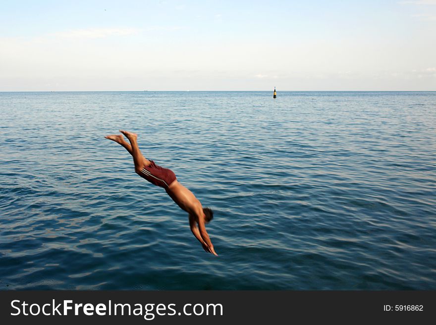 The young man jumping in water from a pier. The young man jumping in water from a pier